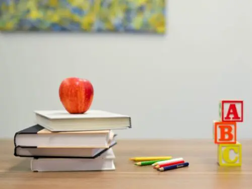 Colored pencils, alphabet blocks, and an apple on top of a stack of books.